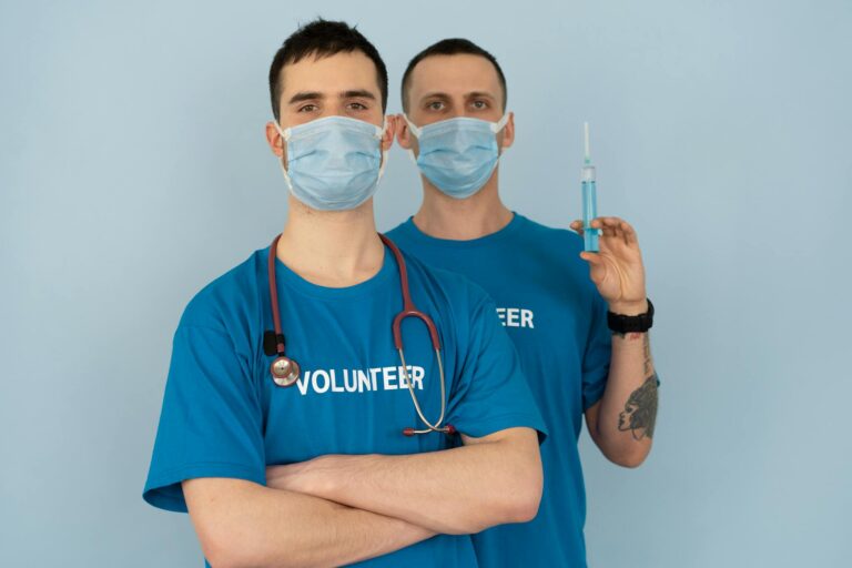 Two medical volunteers wearing masks and uniforms preparing for vaccination.